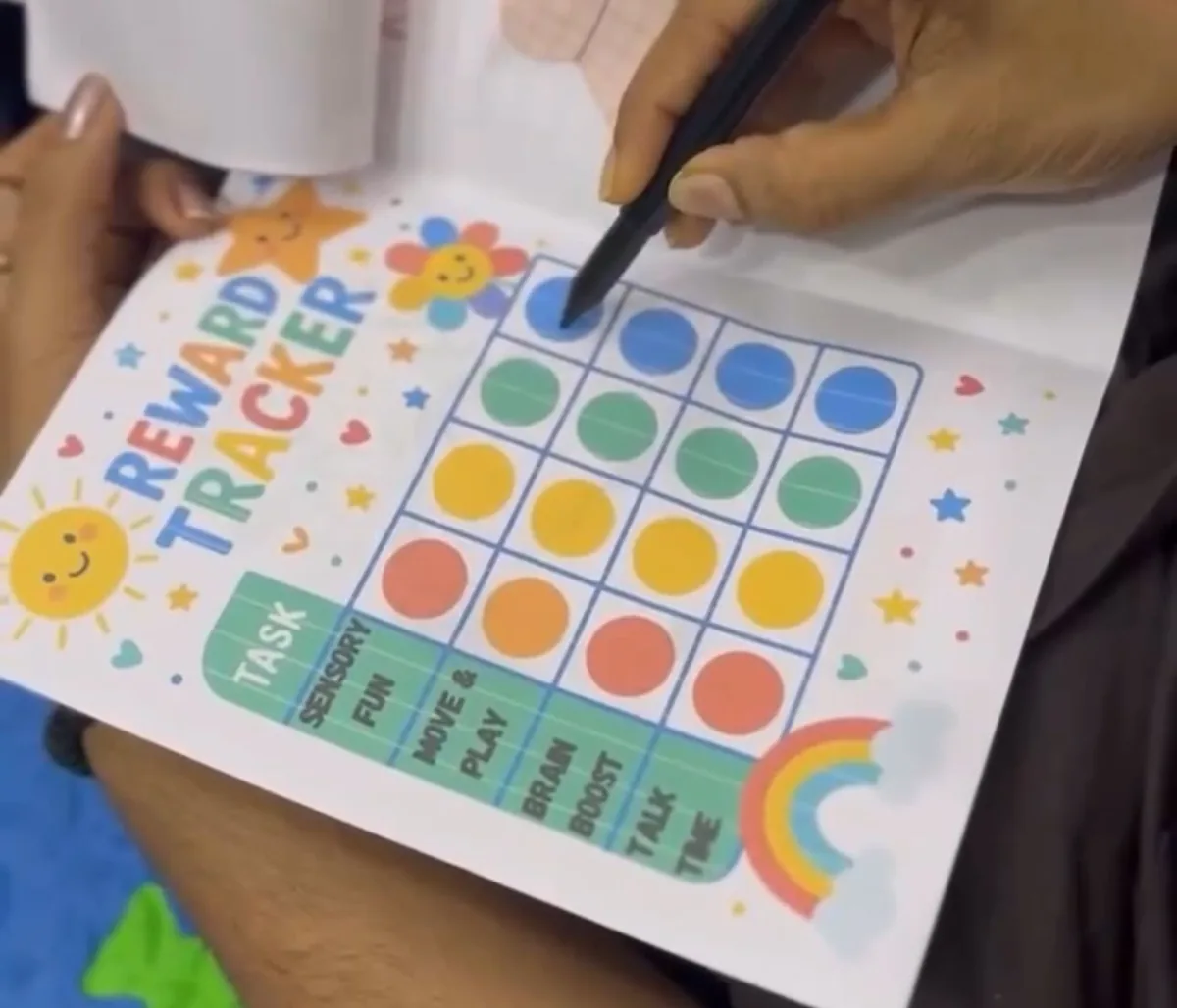 A therapist marks progress on a colourful reward tracker chart